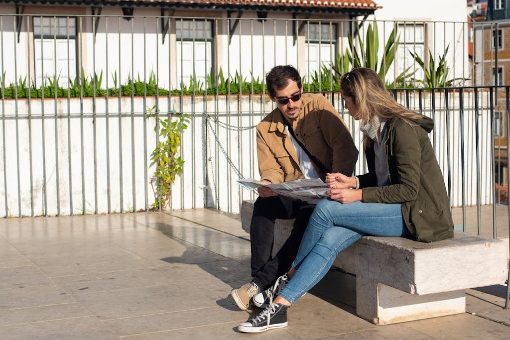 A couple of tourists sitting on a bench, studying a map on a sunny day.